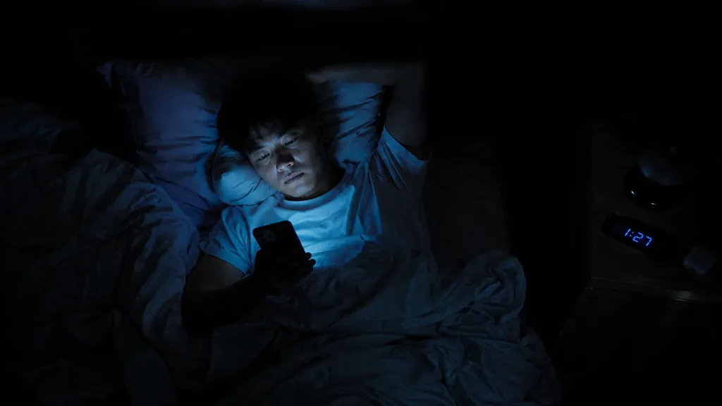Person scrolling phone in dark bedroom at 1:27 AM